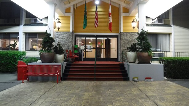 A hotel entrance with a red carpet, steps leading up to a black door, and two large potted plants on either side. - Wingate by Wyndham Mount Vernon (Mount Vernon)