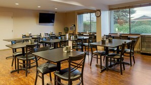 A spacious dining area with multiple tables and chairs, a flat-screen TV mounted on the wall, and large windows providing natural light. - Wingate by Wyndham Mount Vernon (Mount Vernon)