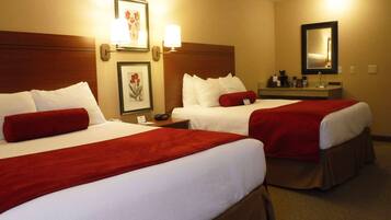 A hotel room with two beds, each with white linens and red accents, a bedside table with a lamp, a framed picture on the wall, and a mirror above the table.
