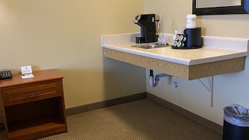 A hotel bathroom with a sink, a coffee maker, a trash can, and a small wooden nightstand.