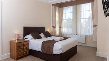 A neatly made bed with a headboard, a bedside table with a lamp, and a window with curtains.