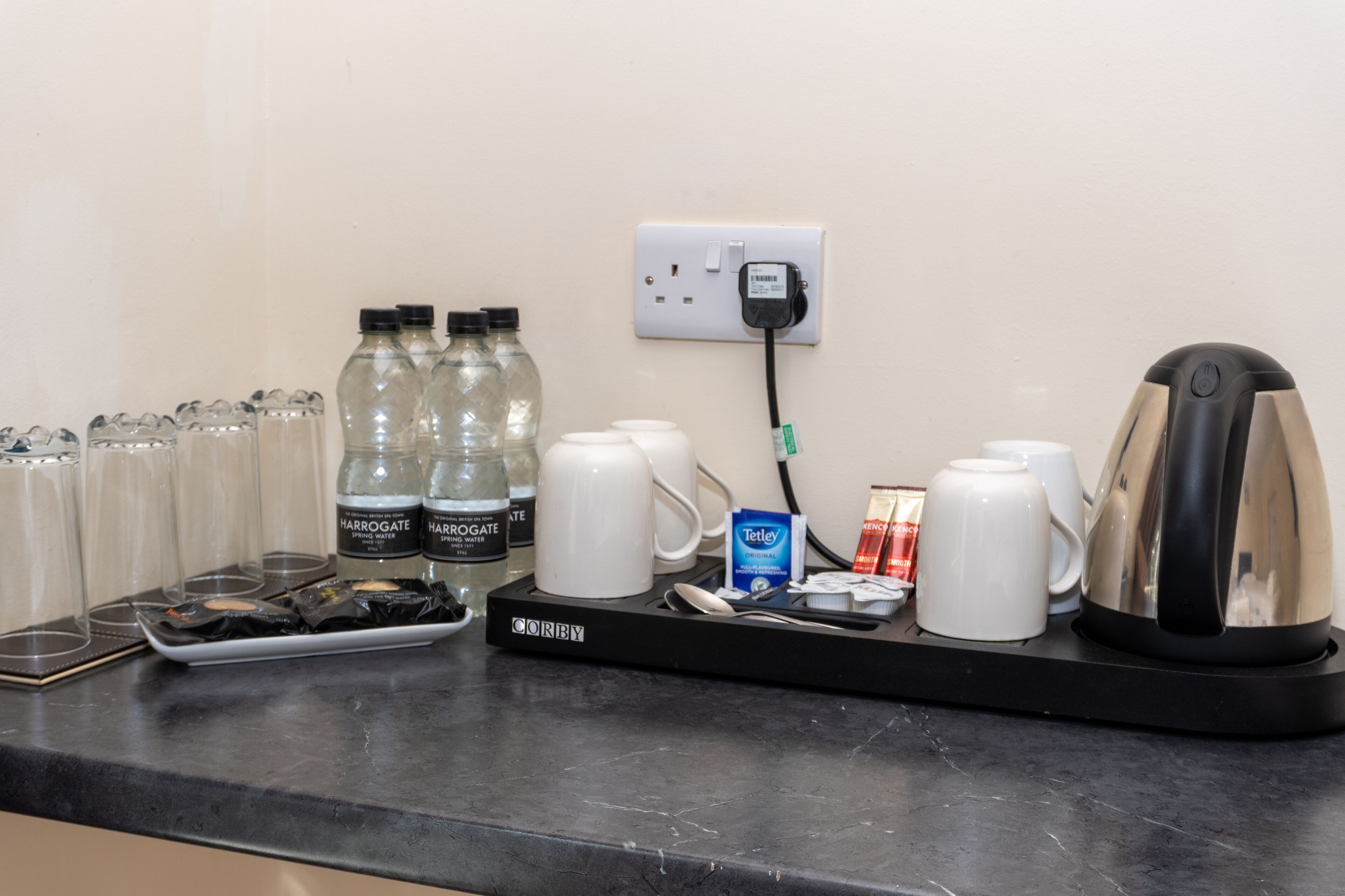 A coffee station with a coffee maker, cups, sugar packets, and bottled water.