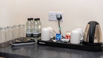 A coffee station with a coffee maker, cups, sugar packets, and bottled water.