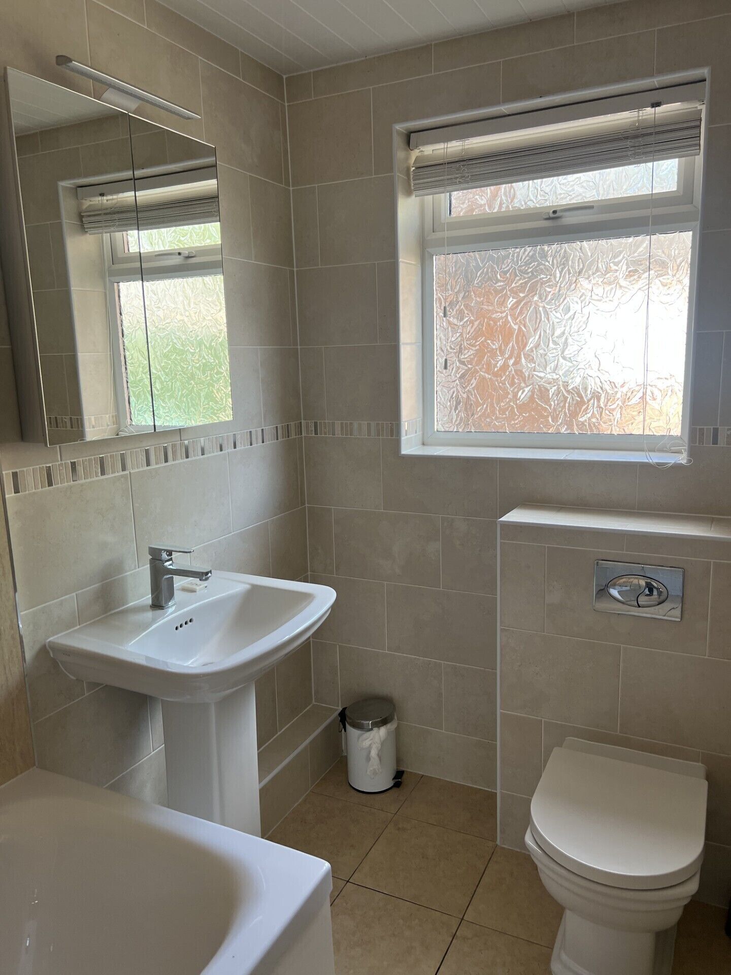 A bathroom with a sink, mirror, toilet, and window with frosted glass.
