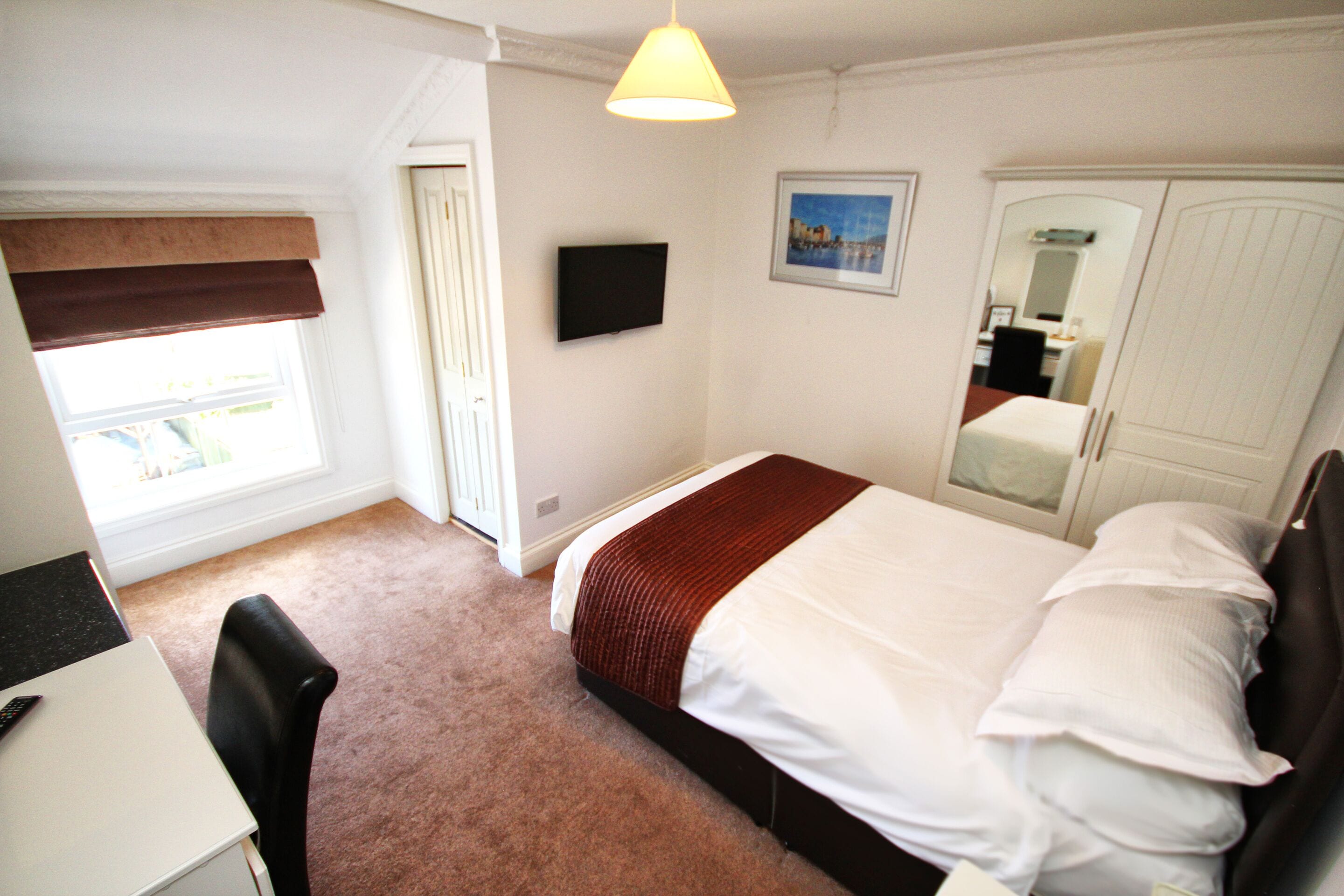 A bedroom with a bed, a desk, a chair, a television, and a wardrobe.
