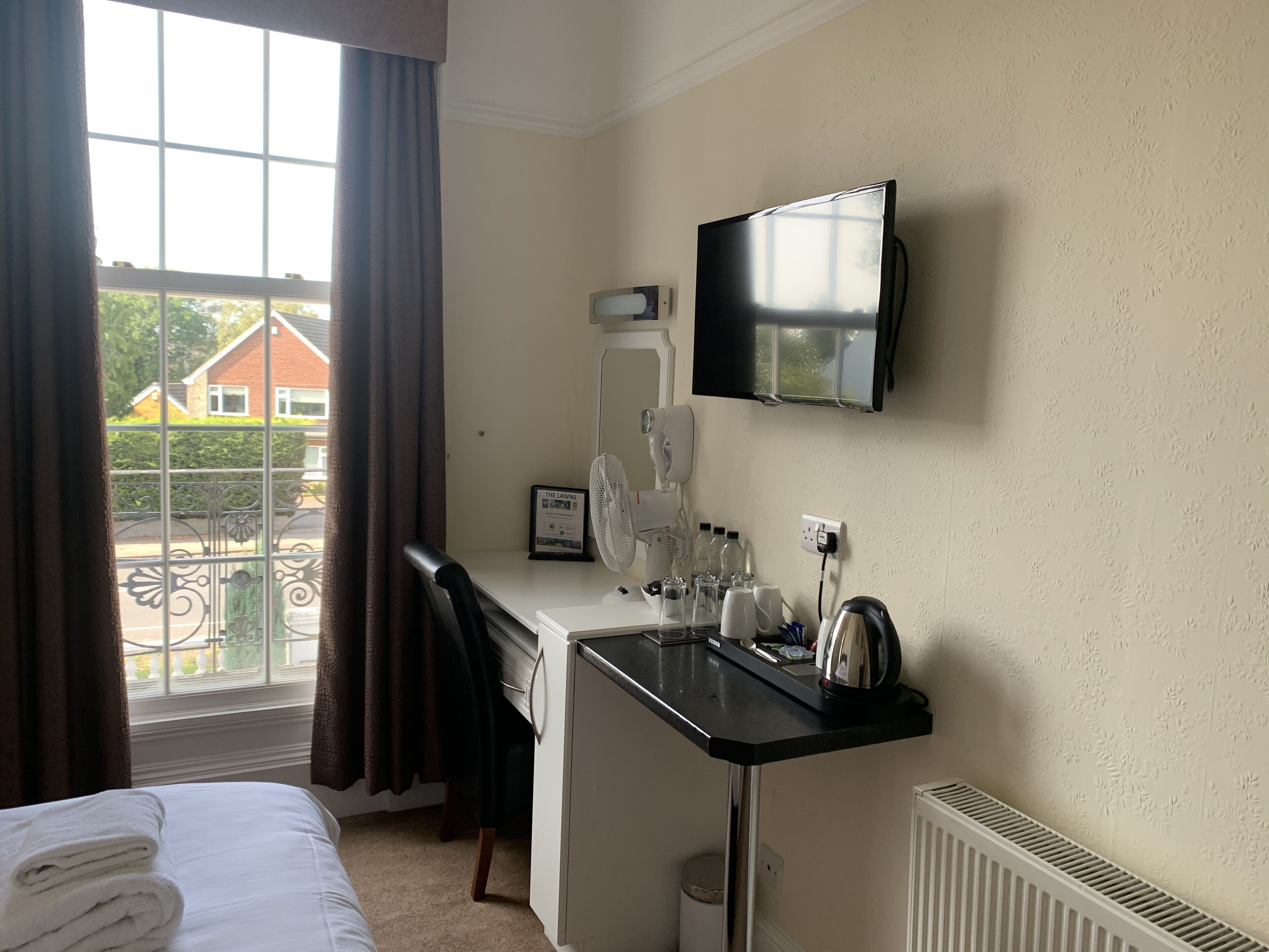 Ein Hotelzimmer mit Bett, Schreibtisch mit Spiegel, Fernseher und Fenster mit Vorhängen.