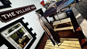 L’auberge du village, avec son panneau indicateur, un banc en bois et une table à l’extérieur.