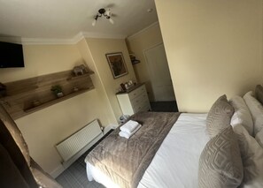 A bedroom with a bed, a dresser, a radiator, a shelf with plants, and a painting on the wall.