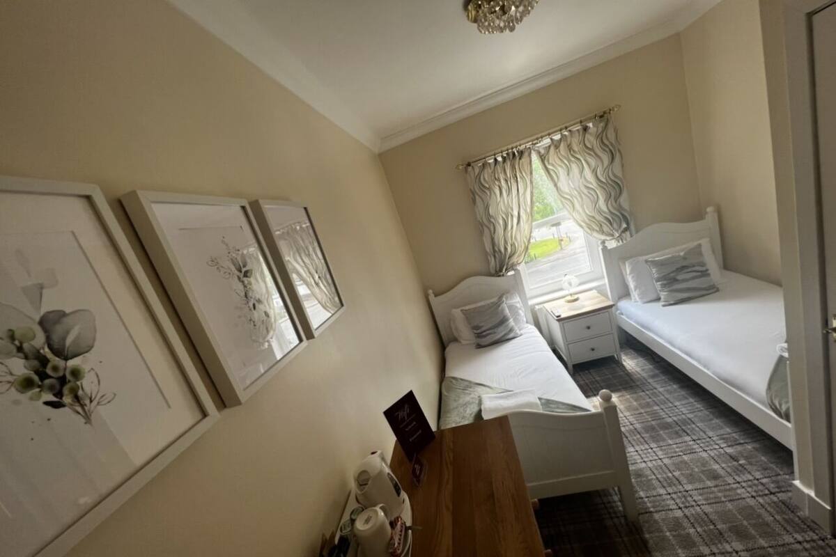 A bedroom with two beds, a wooden desk, and framed artwork on the walls.