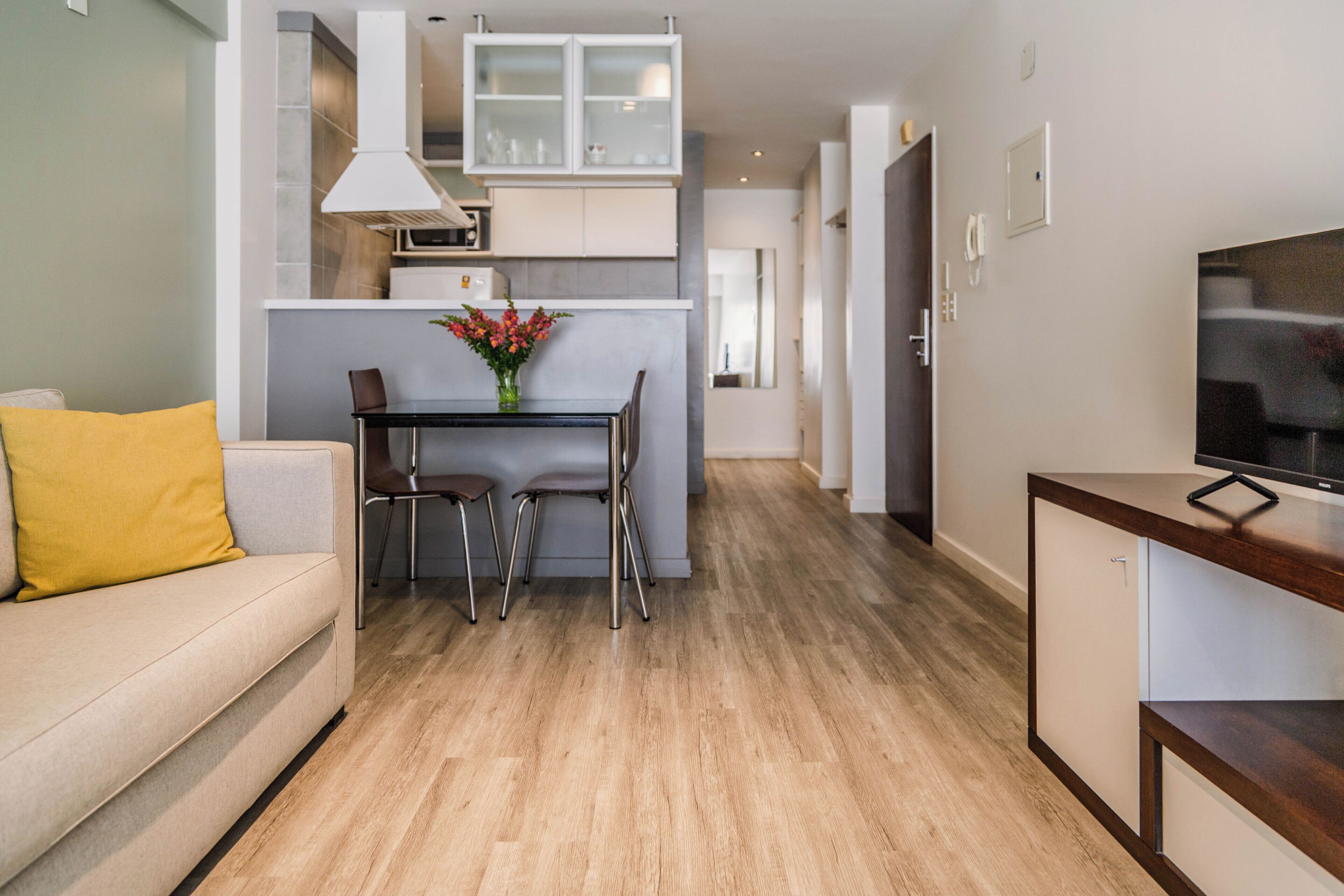 A modern living room with a sofa, a dining table with chairs, a TV on a stand, and a kitchen in the background.