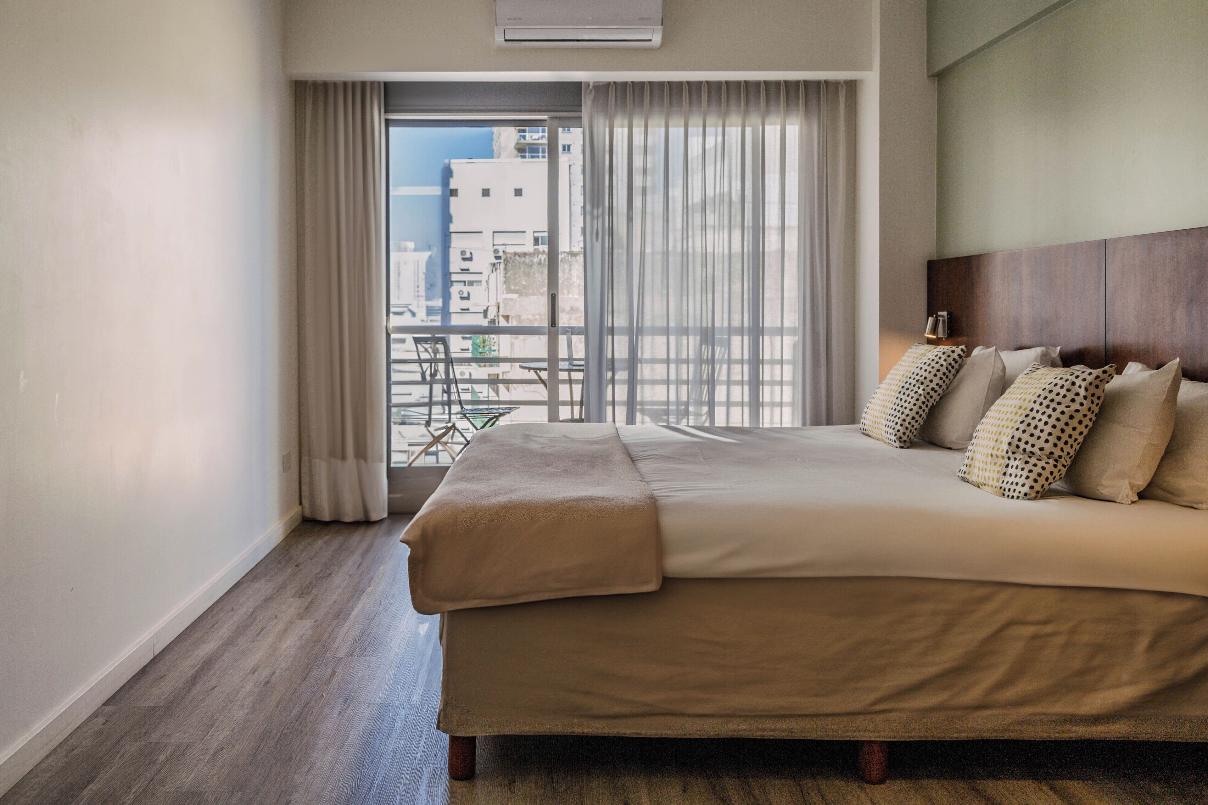 Une chambre d’hôtel dotée d’un grand lit, offrant une vue sur la ville depuis un balcon, et équipée d’un système de climatisation moderne.