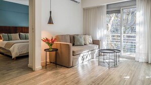 A modern hotel room with a sofa, a small table, a bed, and a large window with curtains. - Color Botanico (Buenos Aires)