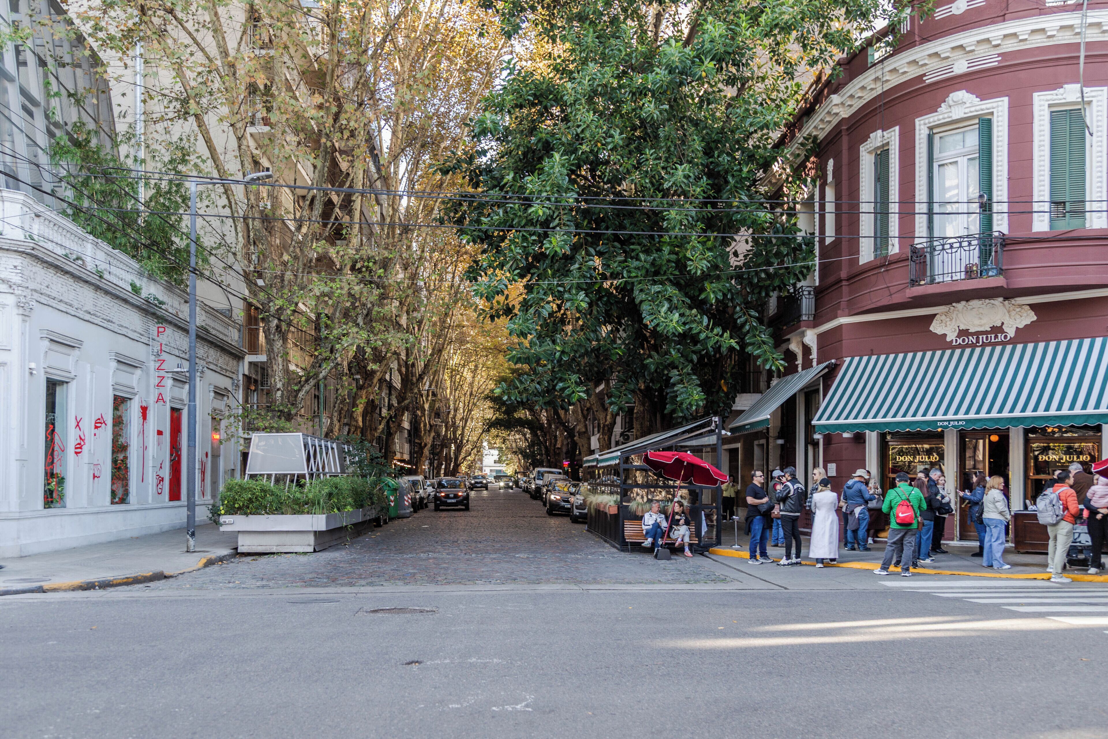 Calle bordeada de árboles y edificios, incluyendo un restaurante llamado 'Don Julio' con toldo verde.