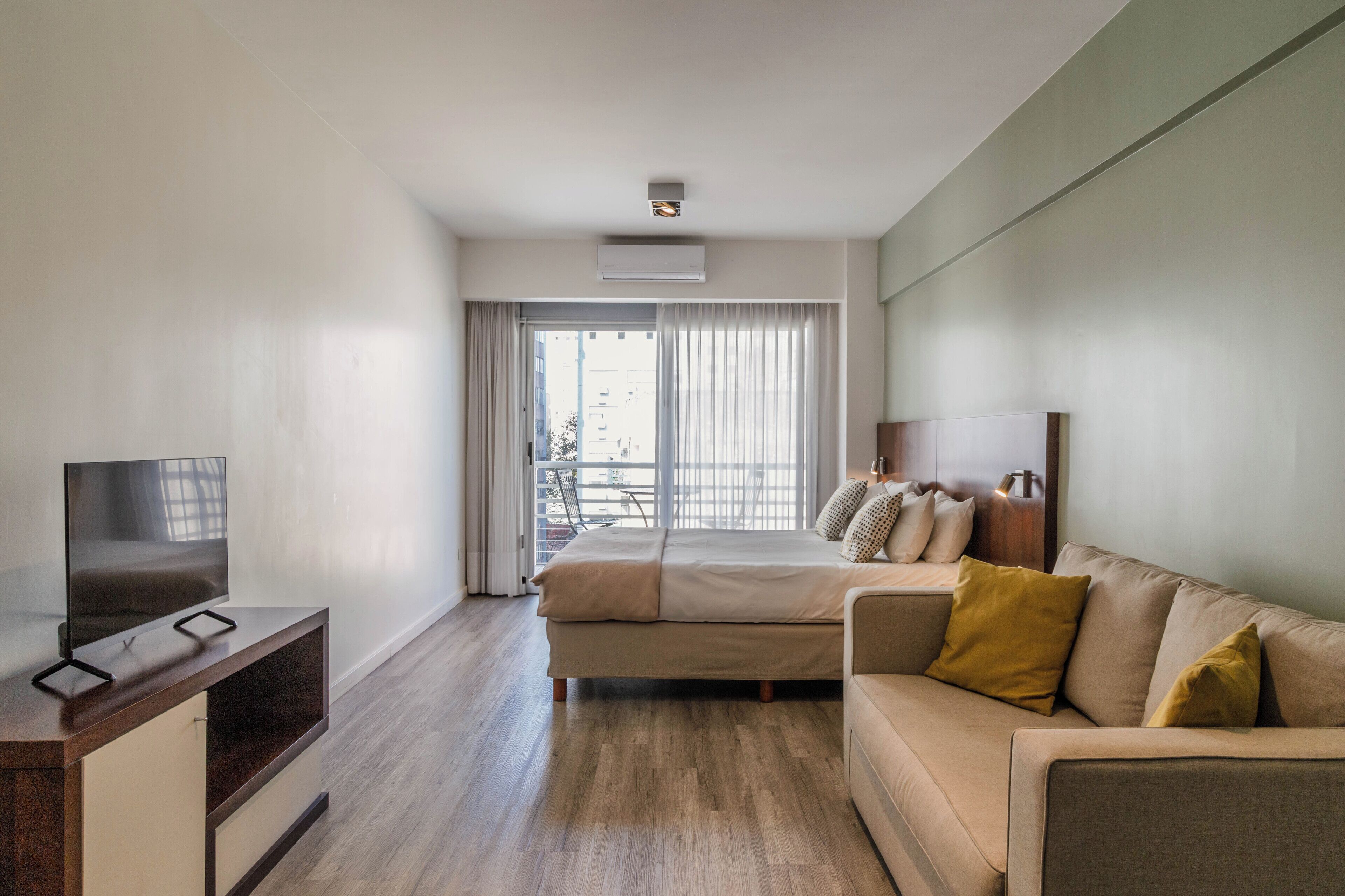 Ein modernes Hotelzimmer mit einem Bett, einer Couch, einem Fernseher und einem Balkon mit Vorhängen.