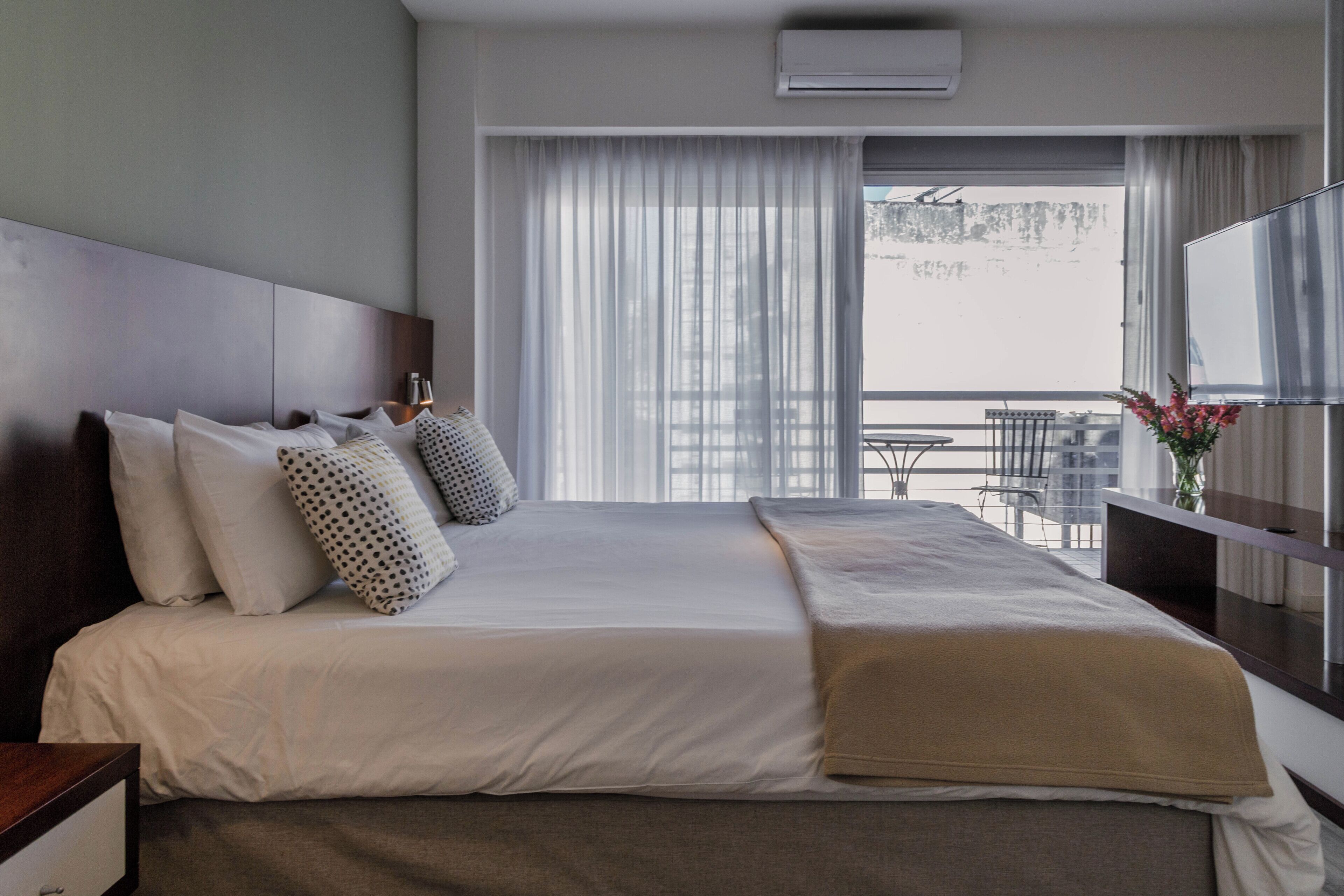 A hotel room with a large bed, a bedside table, a TV, and a balcony with a view.