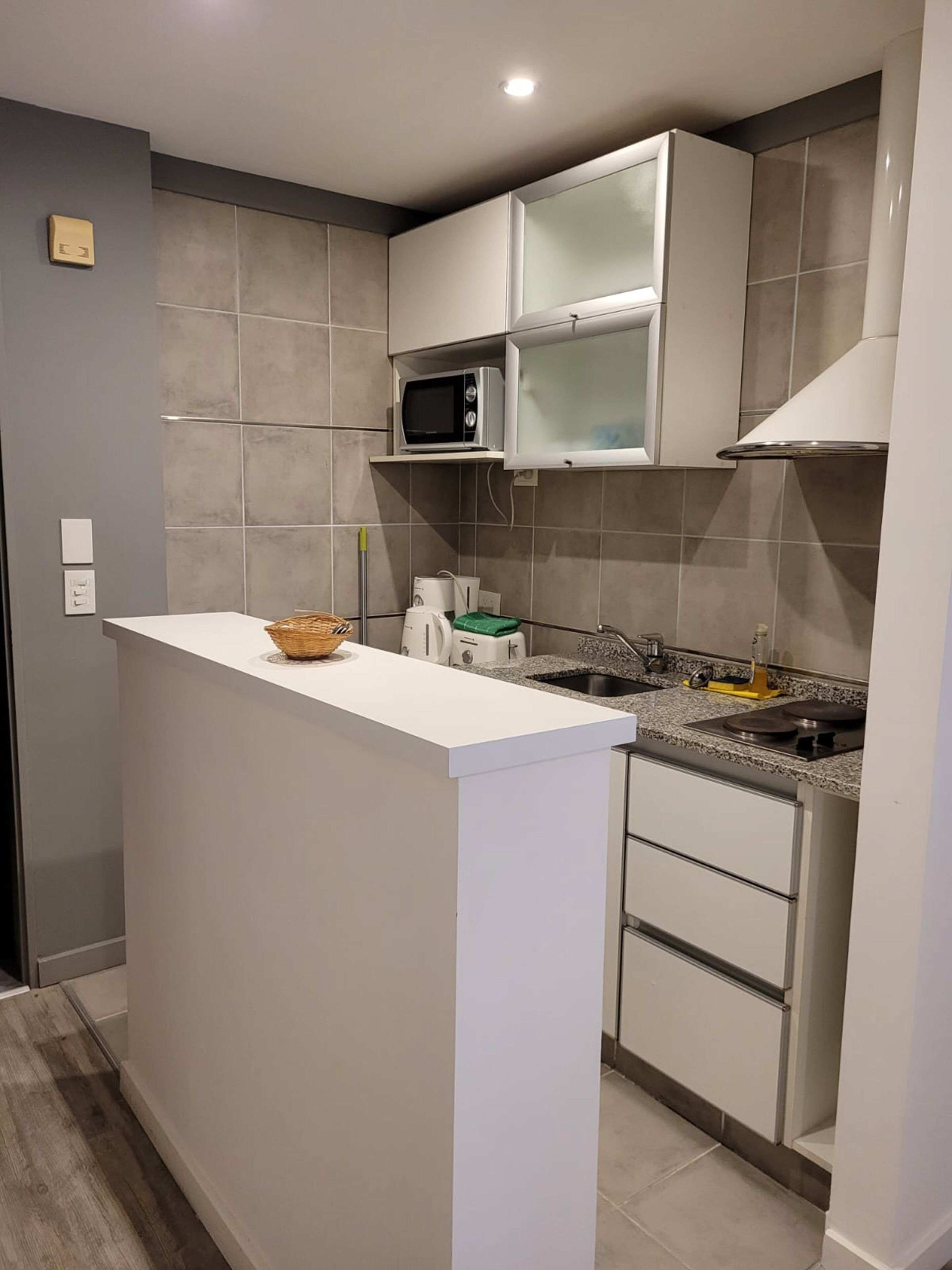 Una cocina compacta con encimera blanca, microondas, fregadero y cocina.