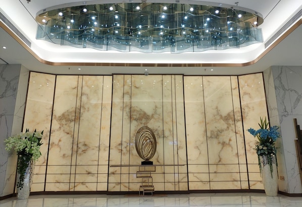 A lobby with a marble wall, a modern light fixture, and two vases with flowers.