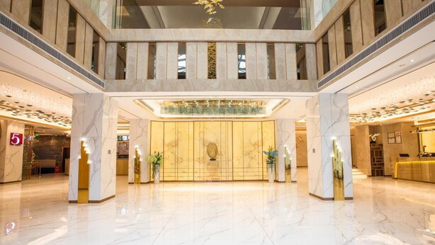 Een ruime lobby met marmeren vloer, een receptiebalie en een hoog plafond met glazen balustrade.