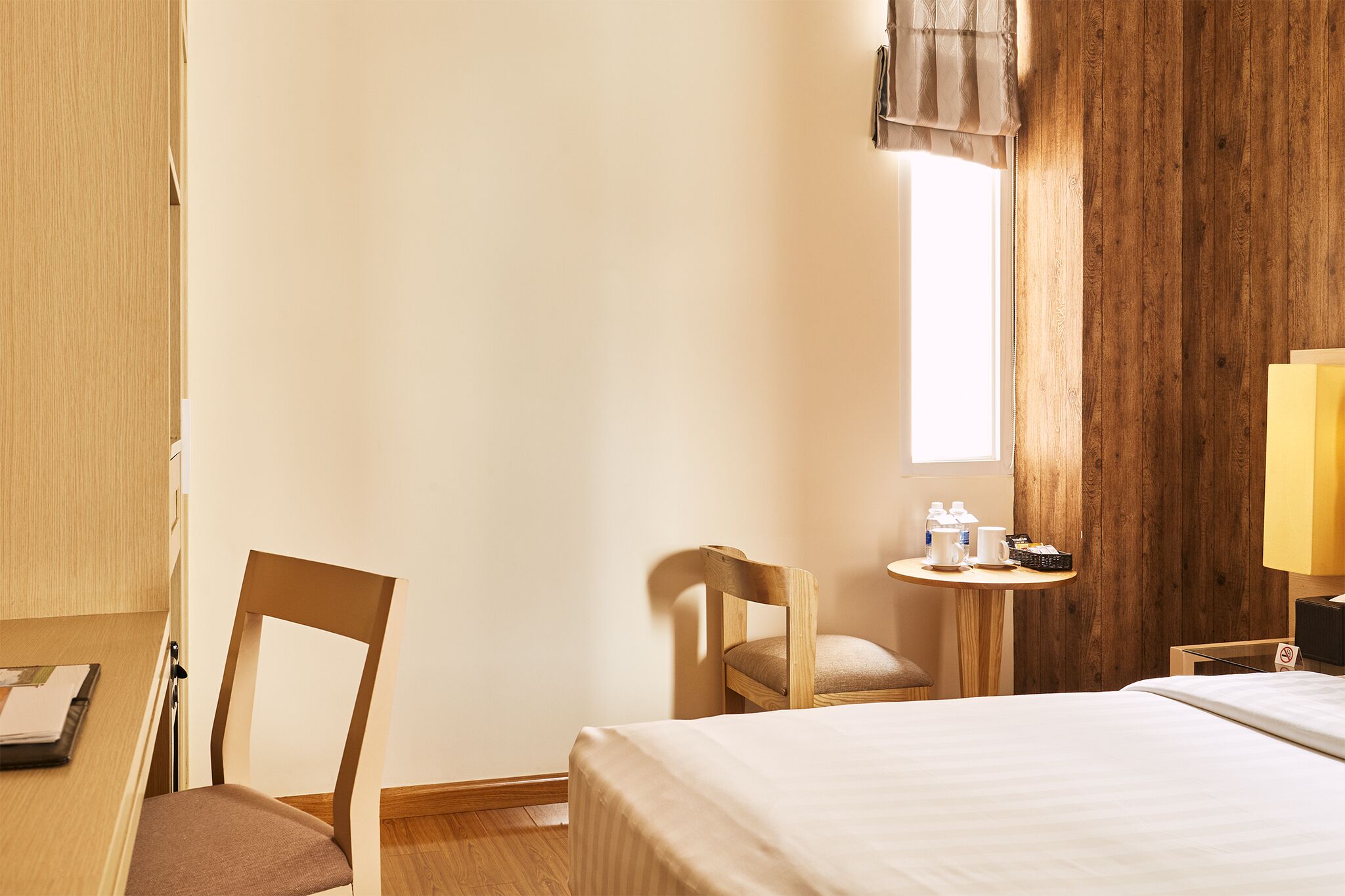 Una camera d'albergo con un letto, due sedie, un tavolino con una lampada e una finestra con tende.