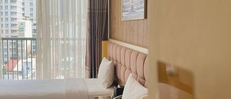 A hotel room with two beds, a wooden headboard, a window with curtains, and a city view.