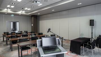 Een vergaderzaal met tafels, stoelen, een laptop, een microfoon en een speaker.