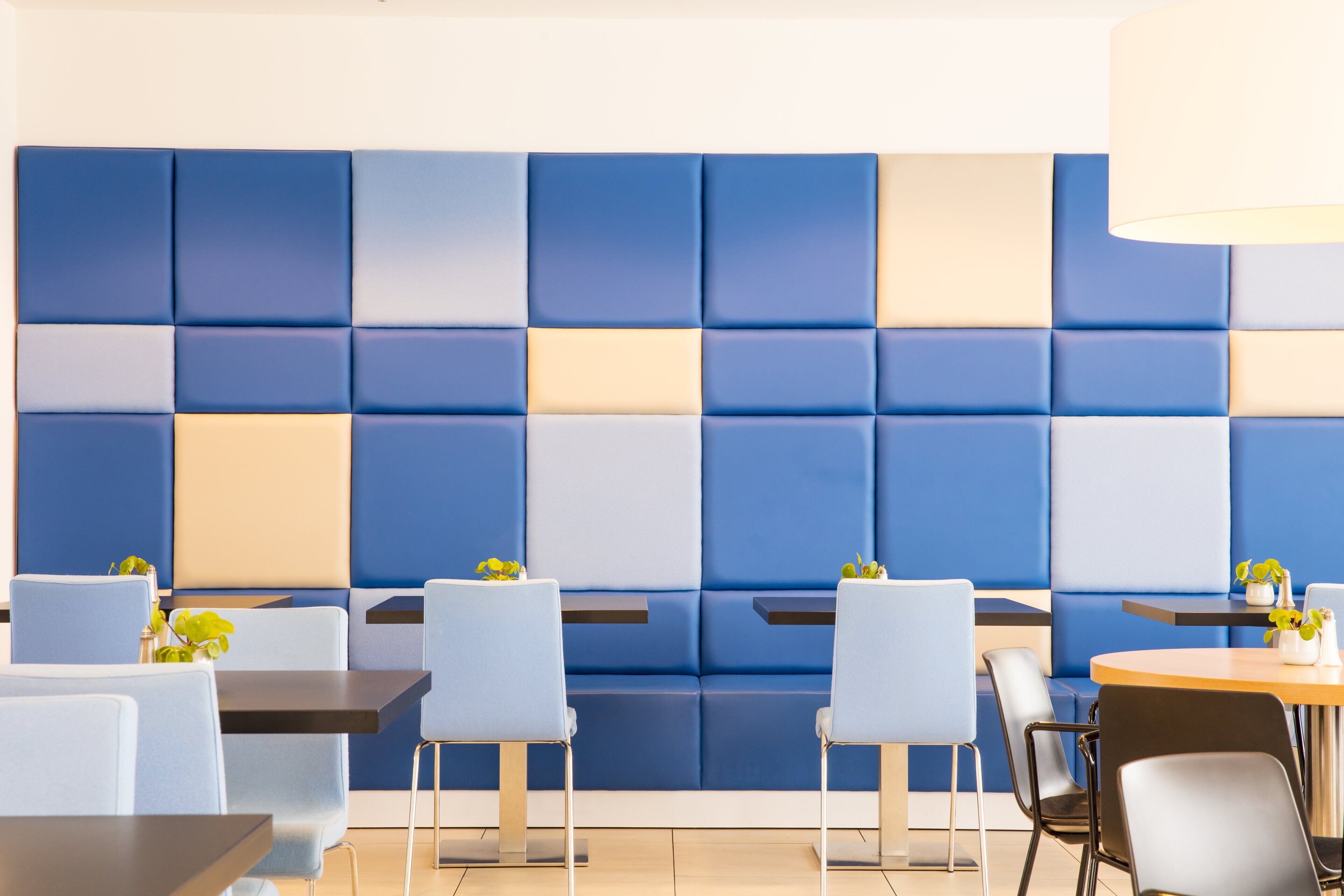 A modern hotel lobby with blue and beige seating, a reception desk, and a plant on the counter.