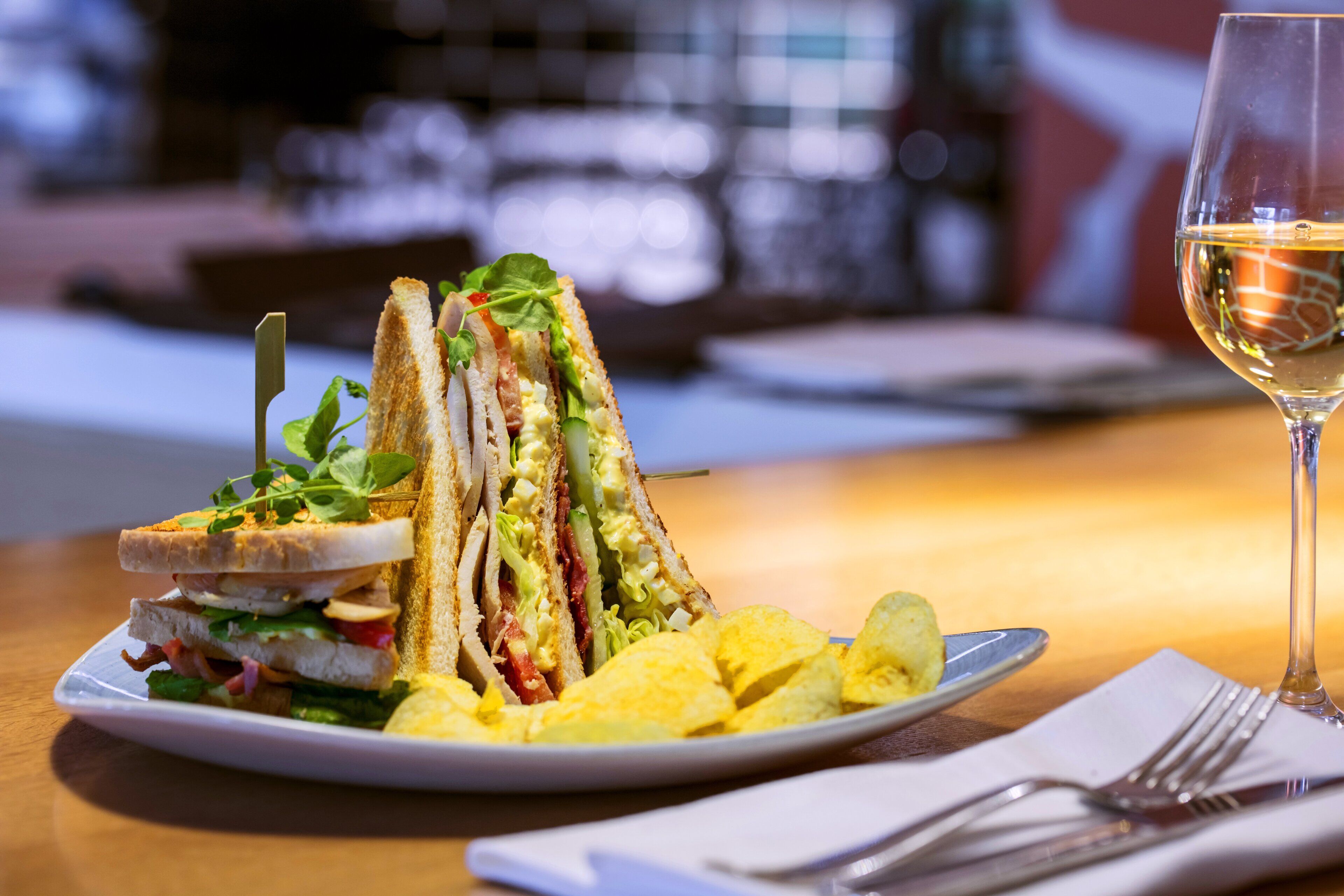 Un sándwich con diferentes ingredientes, una copa de vino blanco y un plato de papas fritas sobre una mesa.