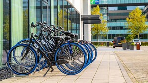 Une rangée de vélos est garée devant un immeuble doté de grandes fenêtres et d’une enseigne indiquant « Holiday Inn Express ».