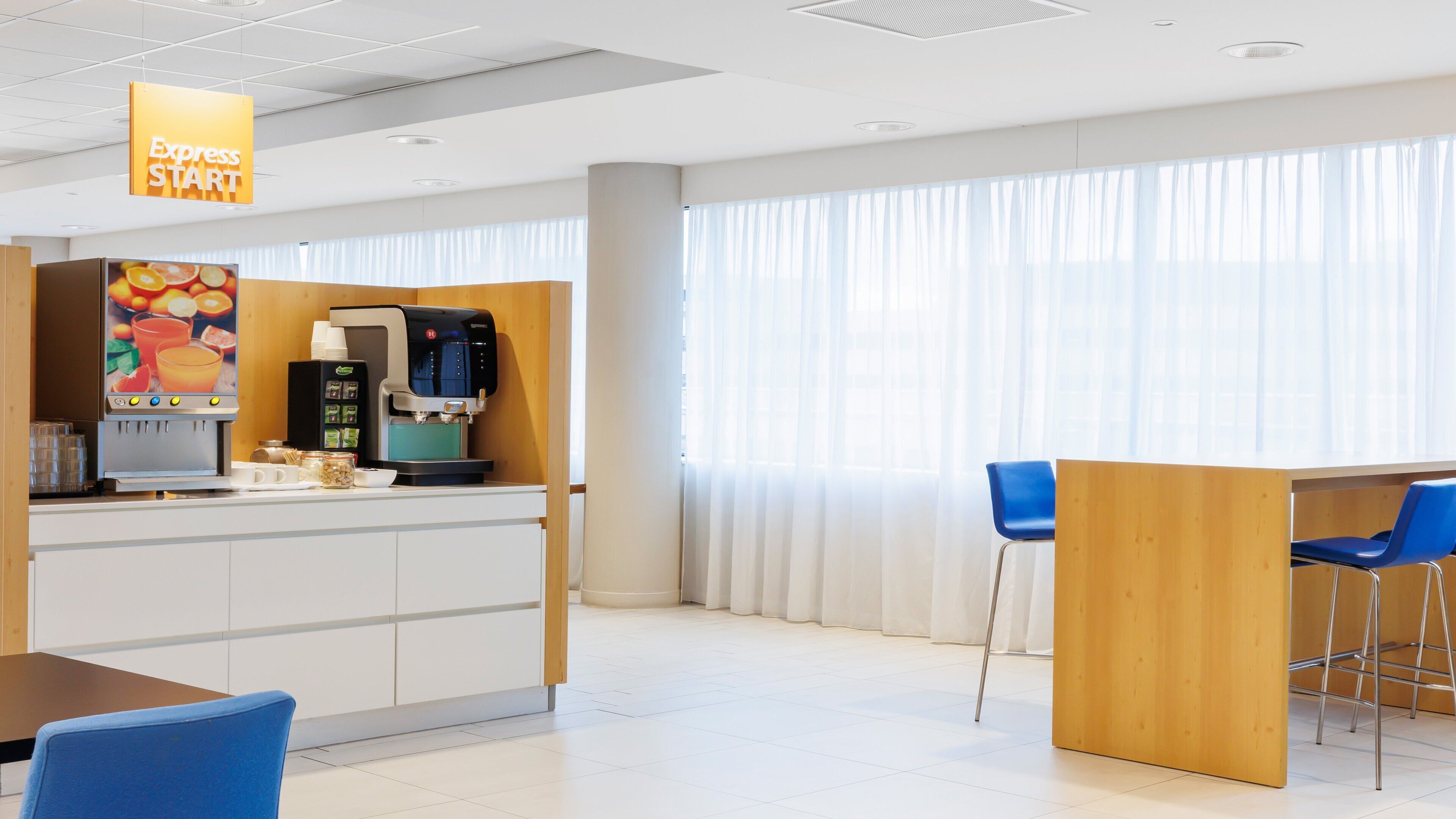 Un hall d’hôtel moderne doté d’un espace café, d’un coin salon et de grandes fenêtres.