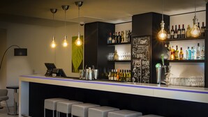 Un espace bar moderne doté d’un long comptoir, de tabourets et d’étagères remplies de bouteilles et de verres.