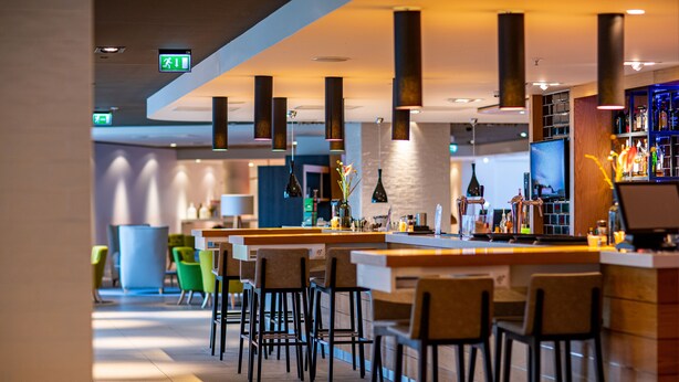 Un espace bar moderne avec des tabourets hauts, un comptoir et des lampes suspendues.