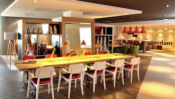 Un espace de salle à manger moderne avec une longue table en bois, des chaises blanches avec des coussins rouges et des luminaires suspendus.