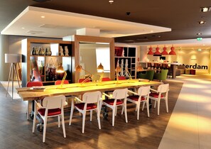 Un comedor moderno con una larga mesa de madera, sillas blancas con cojines rojos e iluminación colgante.