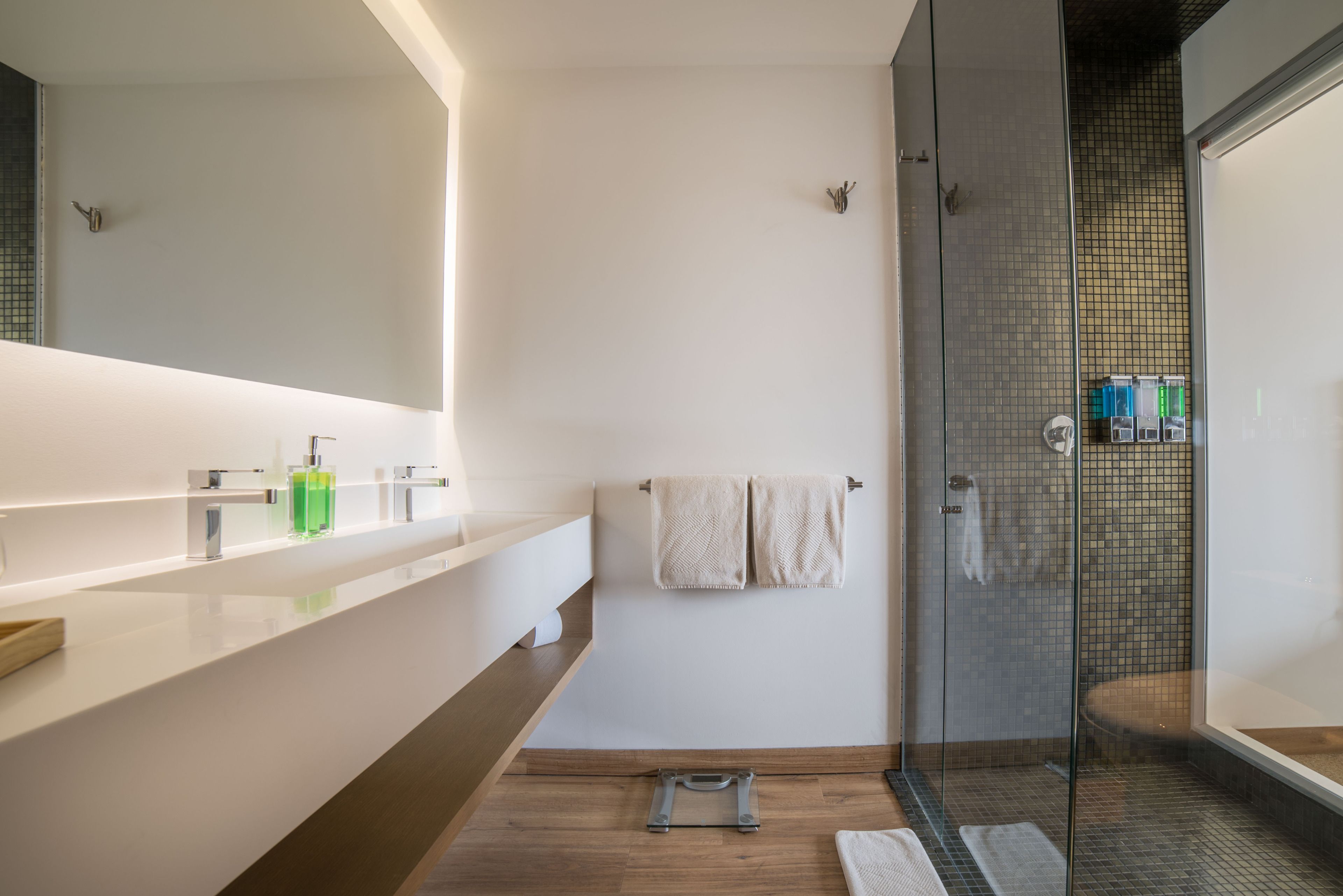 A modern bathroom with a glass shower enclosure, a large mirror, and a wooden vanity.