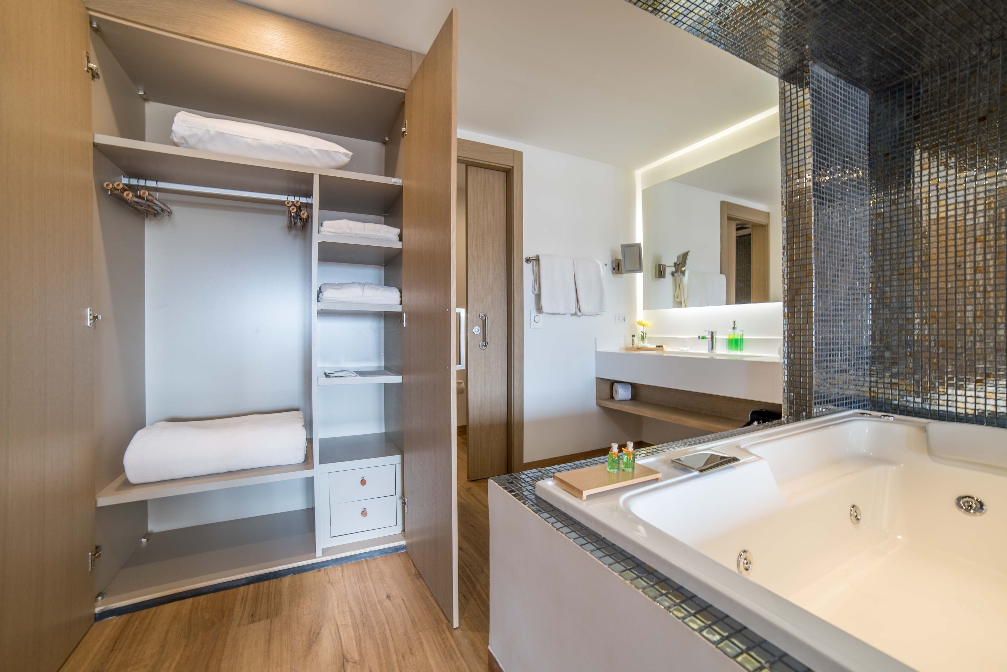 A modern bathroom with a large bathtub, a walk-in shower, and a walk-in closet with shelves and drawers.