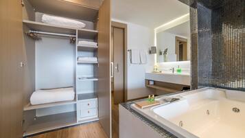 A modern bathroom with a large bathtub, a walk-in shower, and a walk-in closet with shelves and drawers.