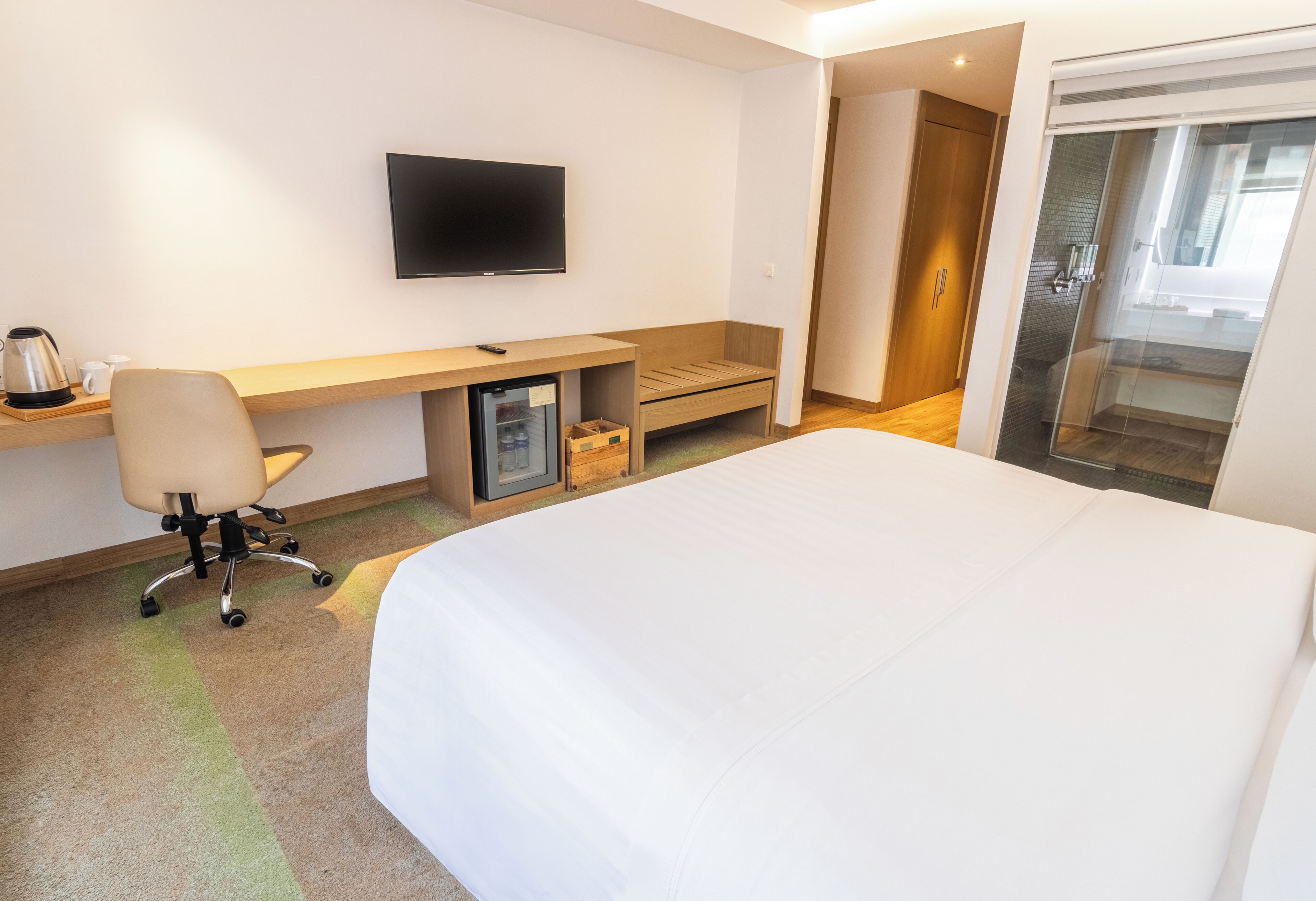 A hotel room with a bed, a desk, a chair, a television, and a sliding door leading to a balcony.