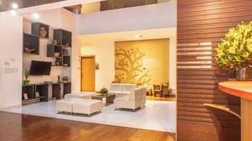 A modern reception area with a wooden reception desk, white sofas, and a wall-mounted TV.