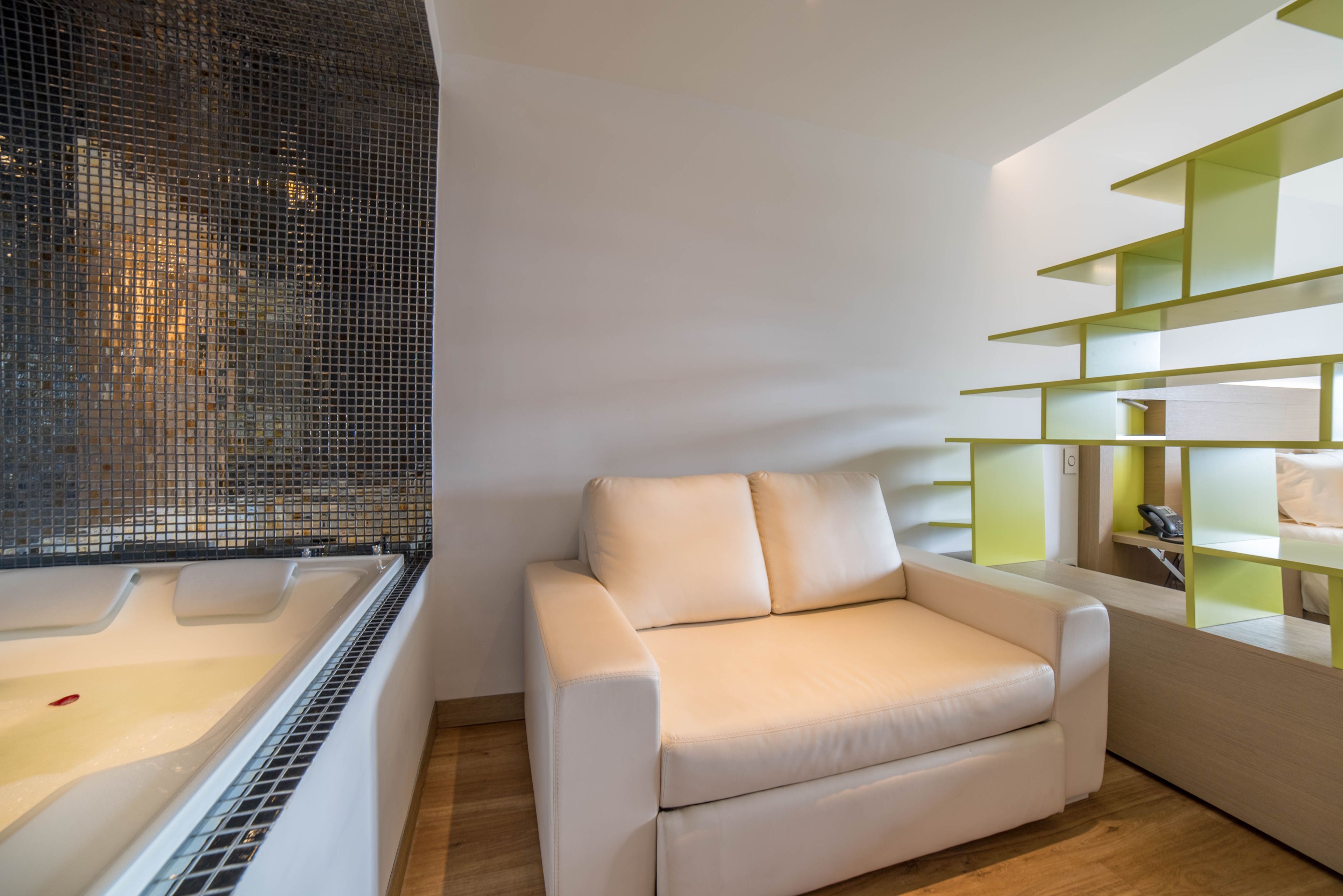 A modern living room with a white sofa, a glass-enclosed bathtub, and a green shelving unit.