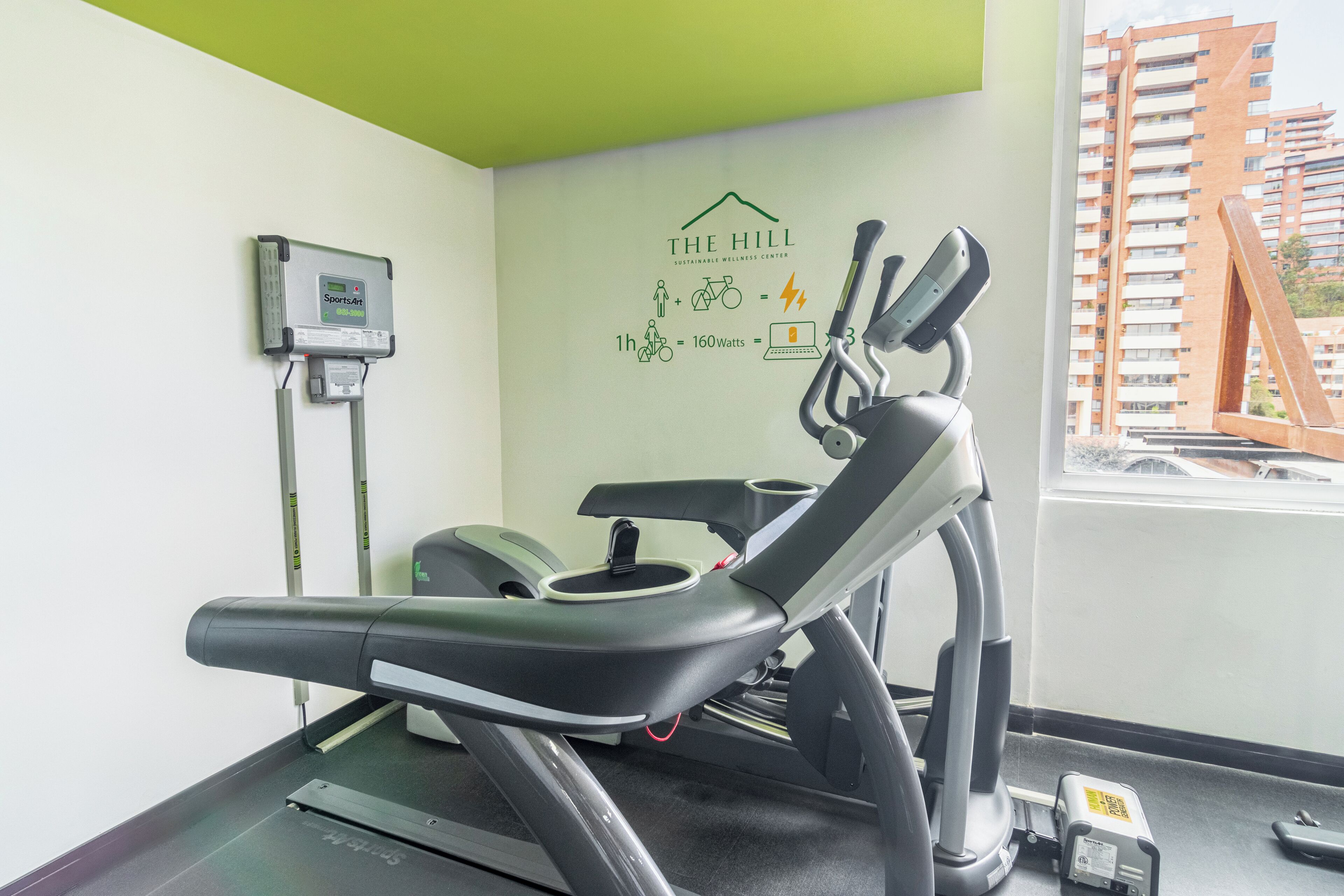 A gym with exercise equipment, a wall-mounted device, and a window with a view of buildings.