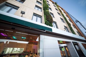 A modern hotel with a green awning, a vertical garden on the facade, and a glass entrance.
