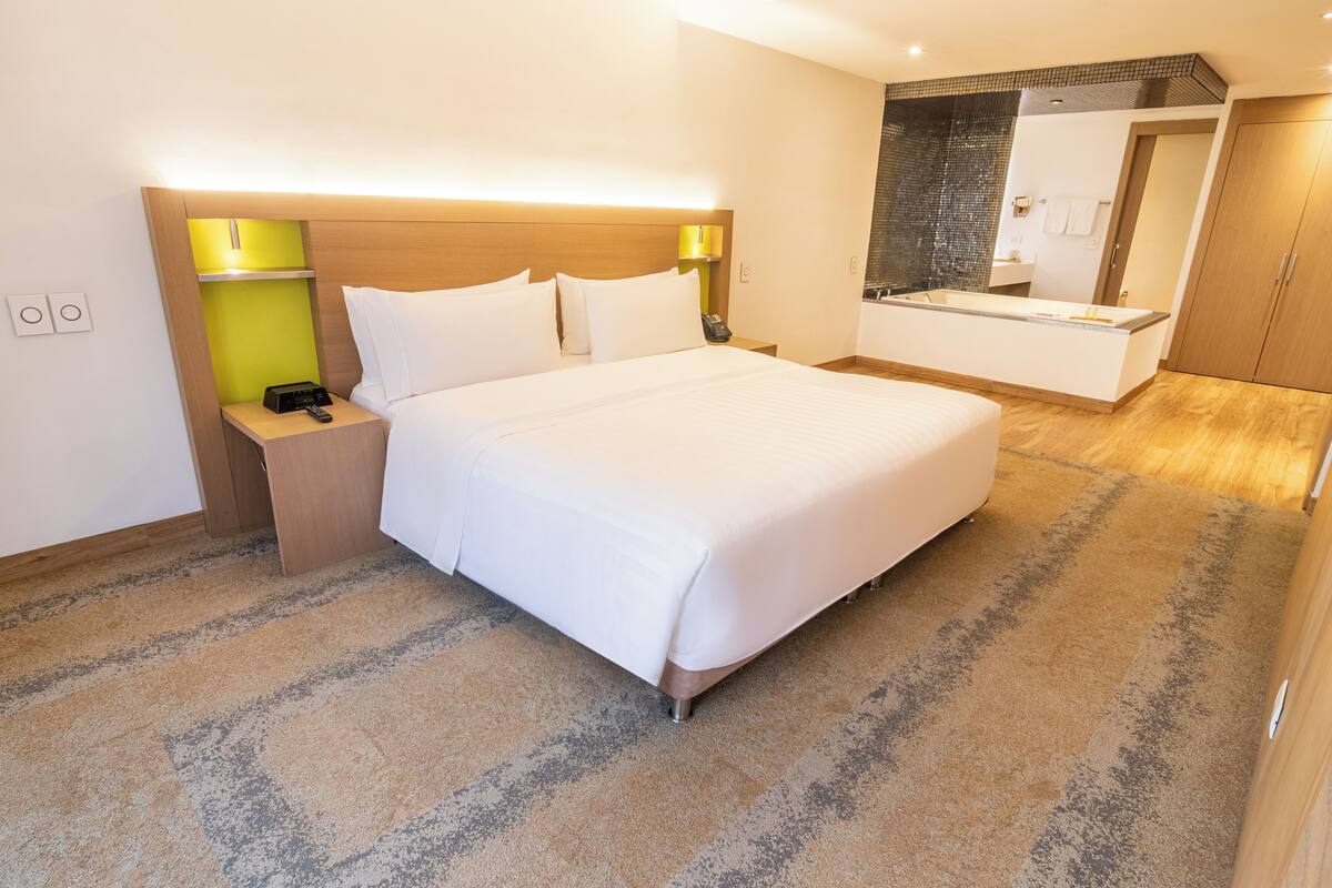 A hotel room with a large bed, bedside lamps, a vanity with a mirror, and a walk-in closet.