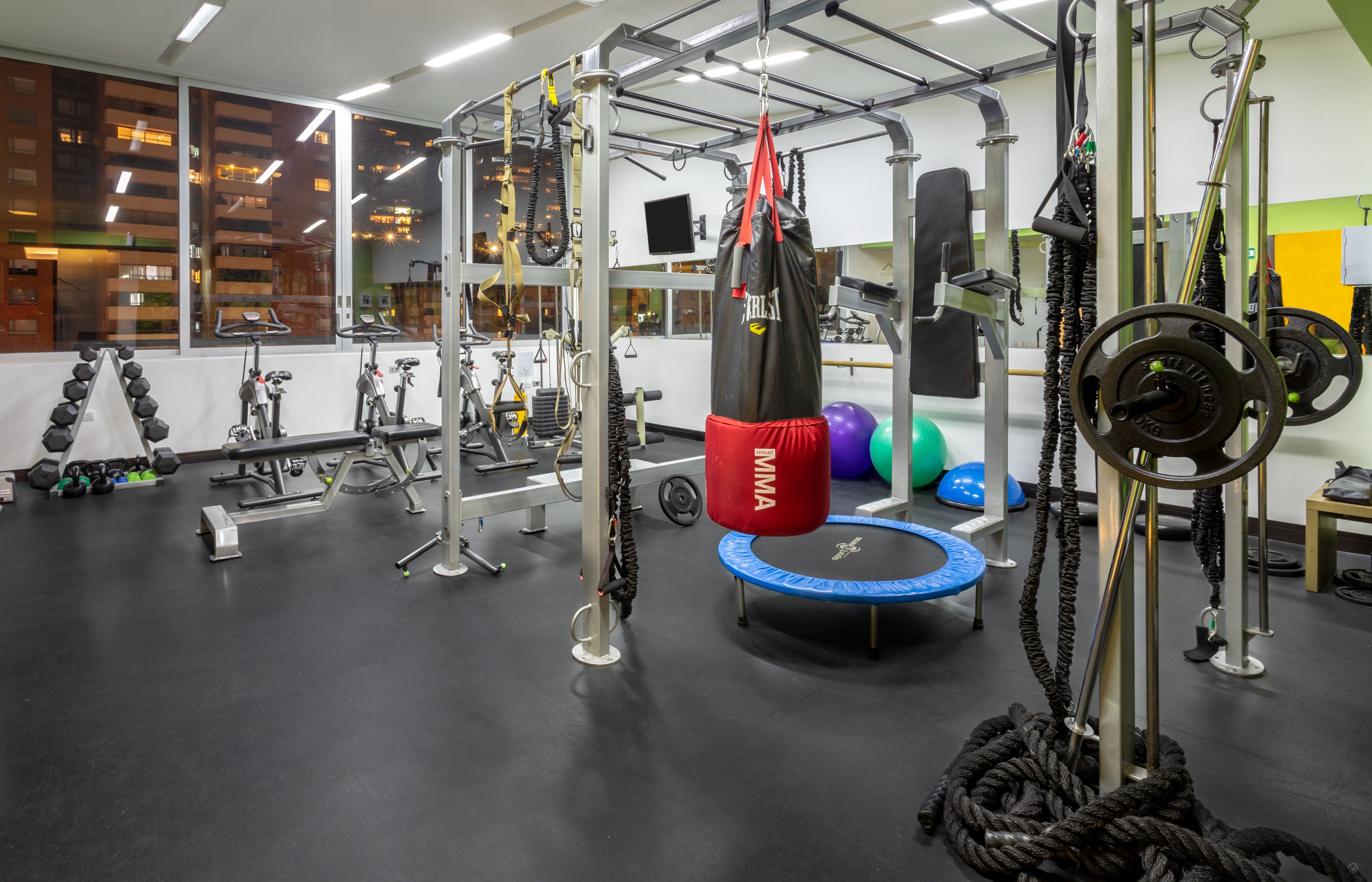 A gym with various exercise equipment, including a punching bag, weight plates, and a trampoline.