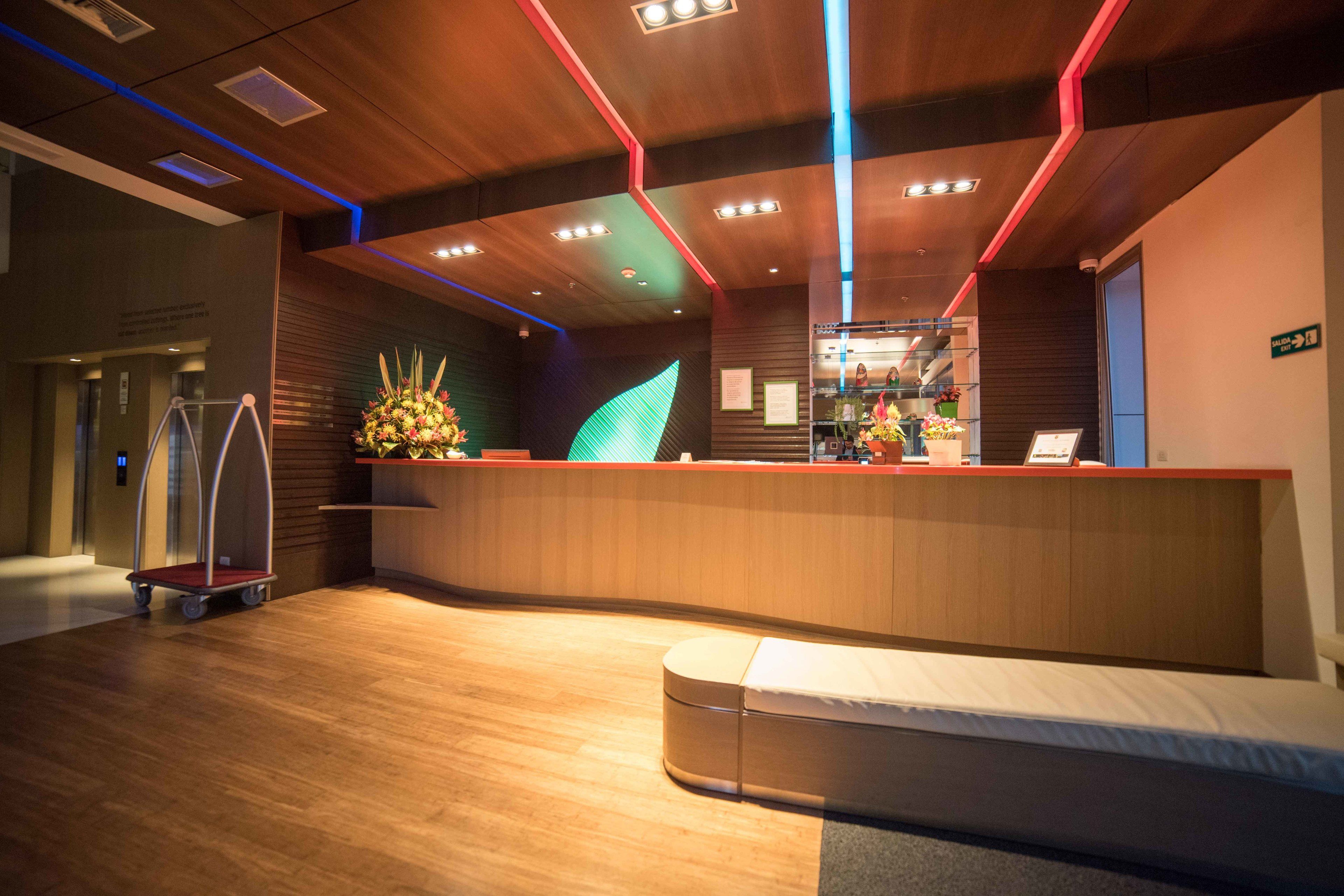 A hotel reception area with a curved wooden reception desk, a seating area, and a floral arrangement.