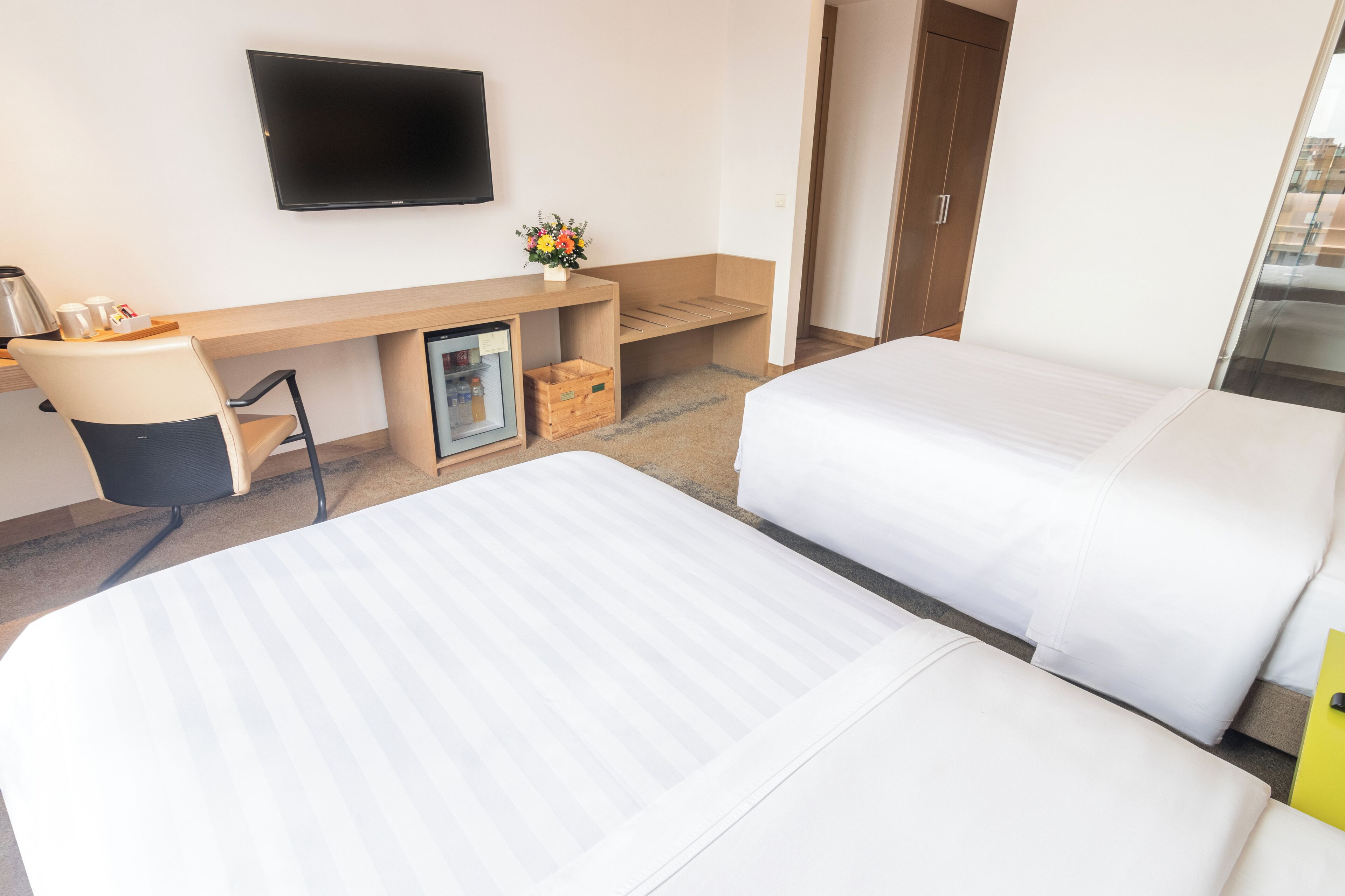 Een hotelkamer met twee bedden, een bureau, een televisie en een kleine koelkast.
