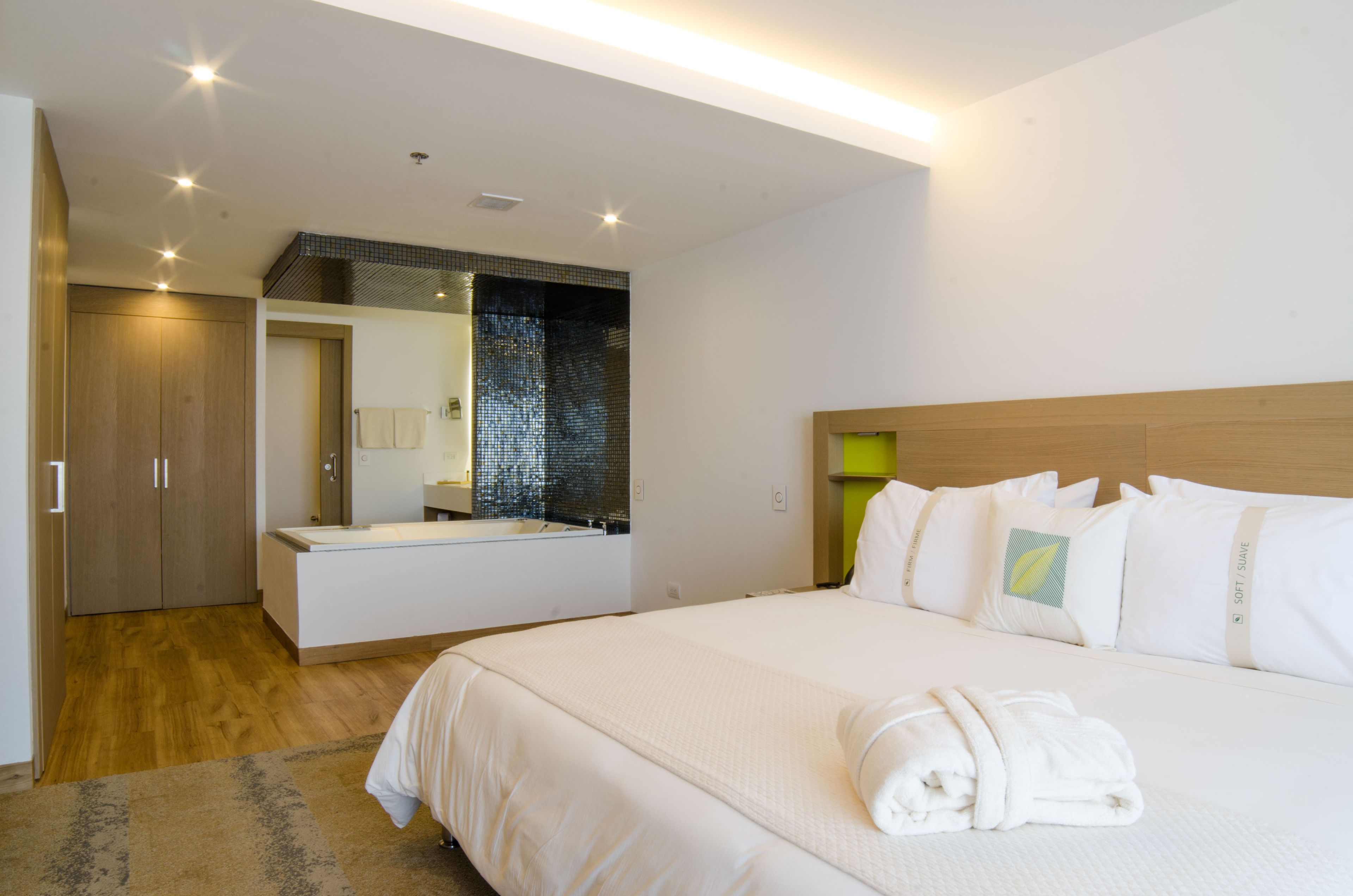 A modern hotel room with a large bed, a bathroom with a mirror, and a wooden wardrobe.