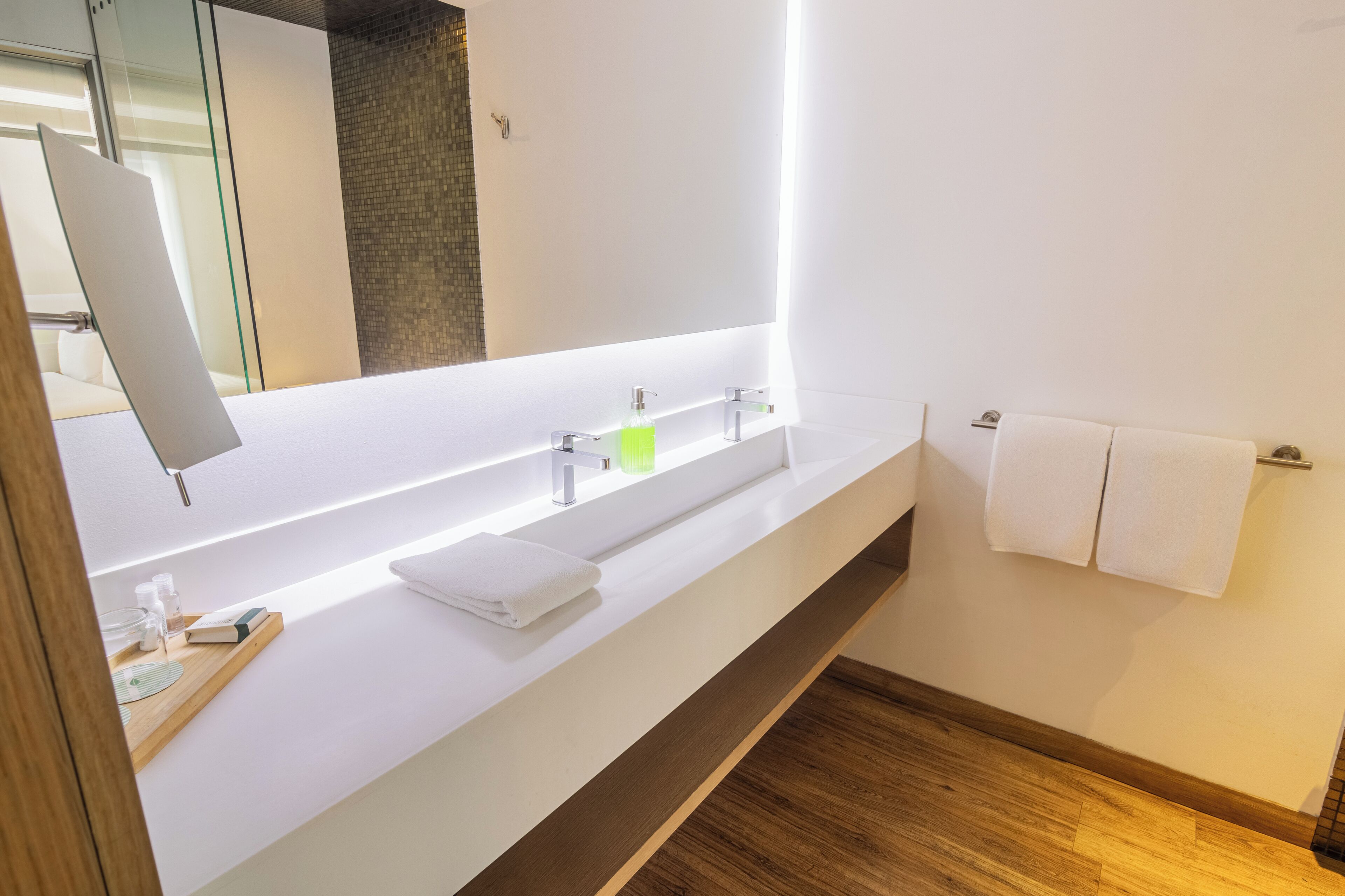 A modern bathroom with a white vanity, two sinks, a large mirror, and a wooden floor.