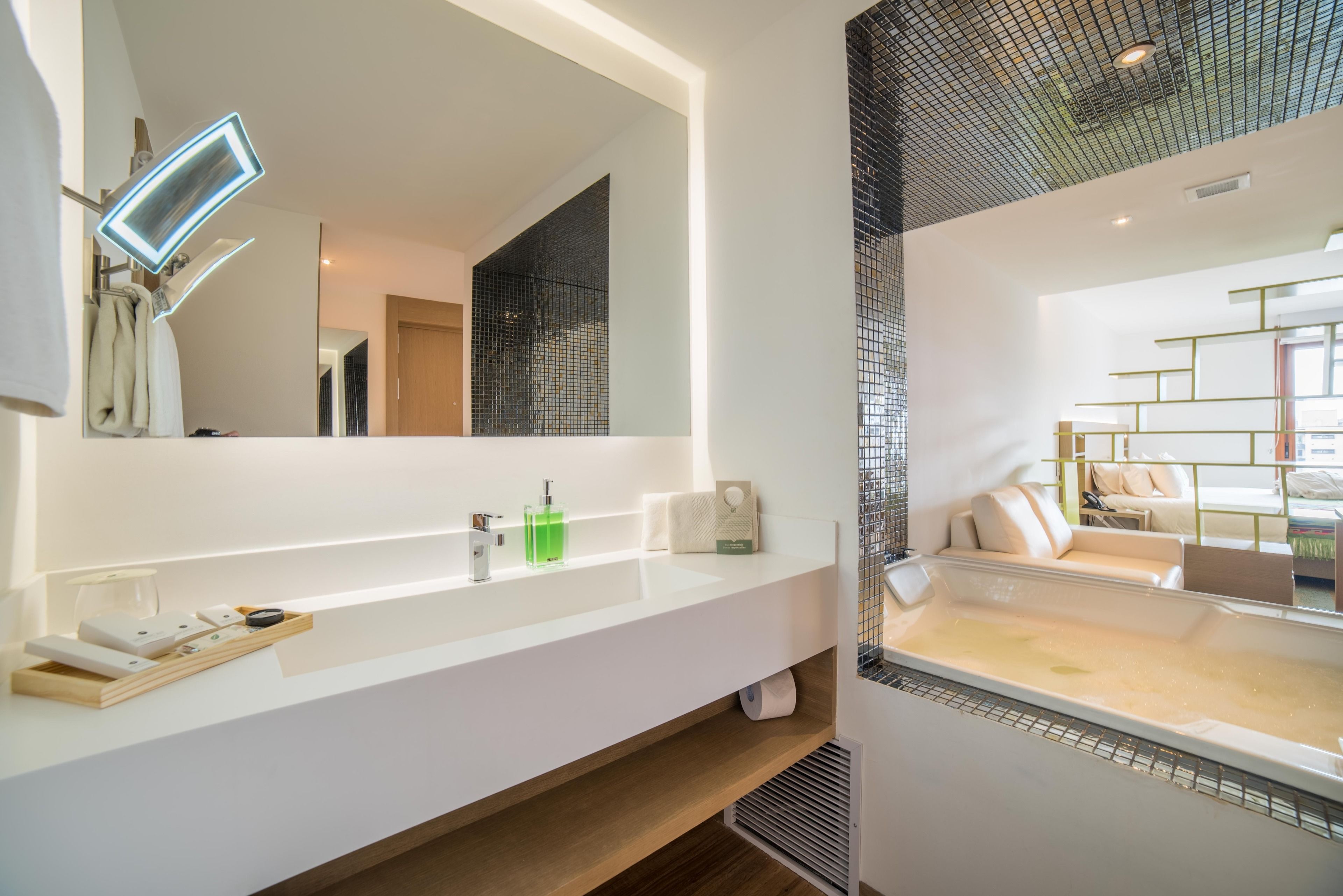A modern bathroom with a large mirror, white countertop, and a bathtub.