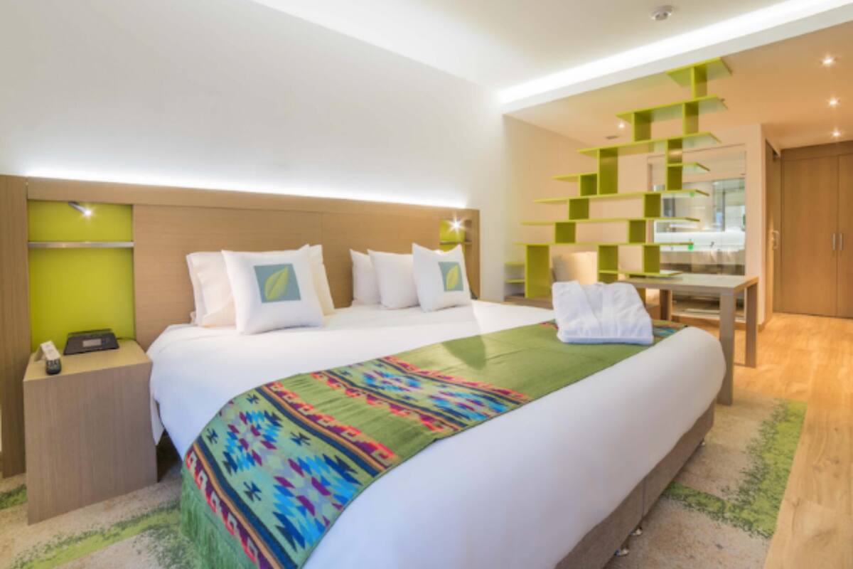 A modern hotel room with a large bed, a desk, and a green accent wall.