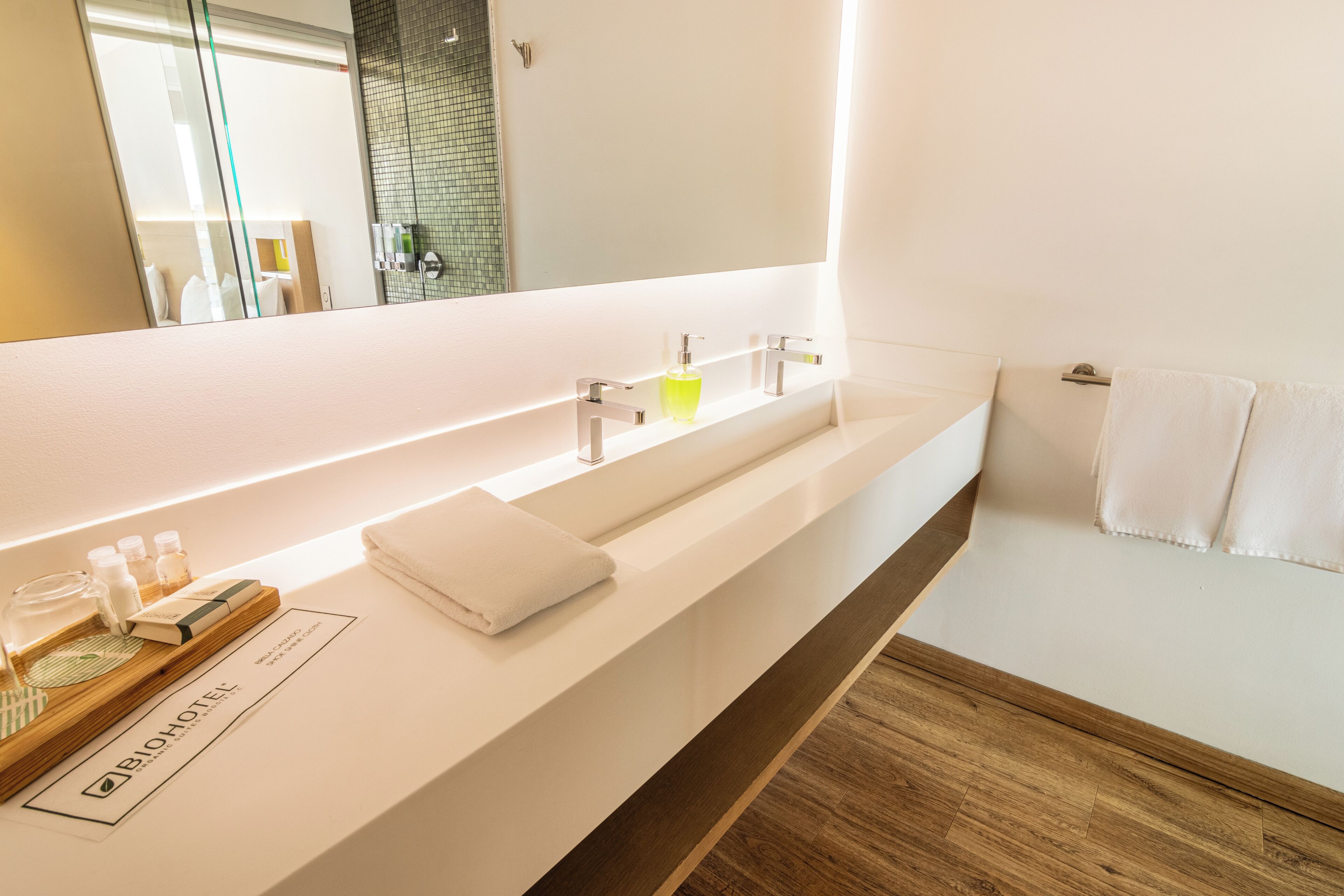 Une salle de bain moderne avec un grand miroir, un plan de toilette blanc et un parquet en bois.